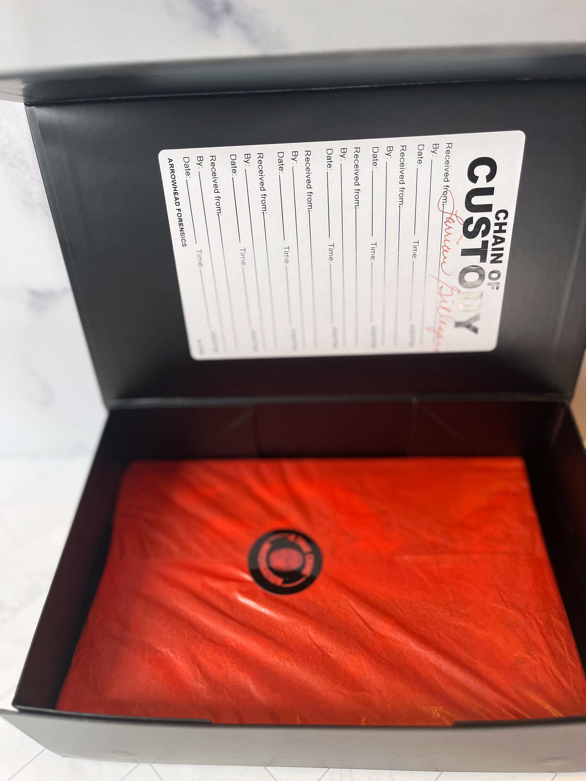 A sleek black box featuring a “Chain of Custody” form on the lid and a red-wrapped item stamped with a circular black logo inside—this is The Murder Box Edition, meticulously crafted as the 100th Anniversary Houdini collector’s set.