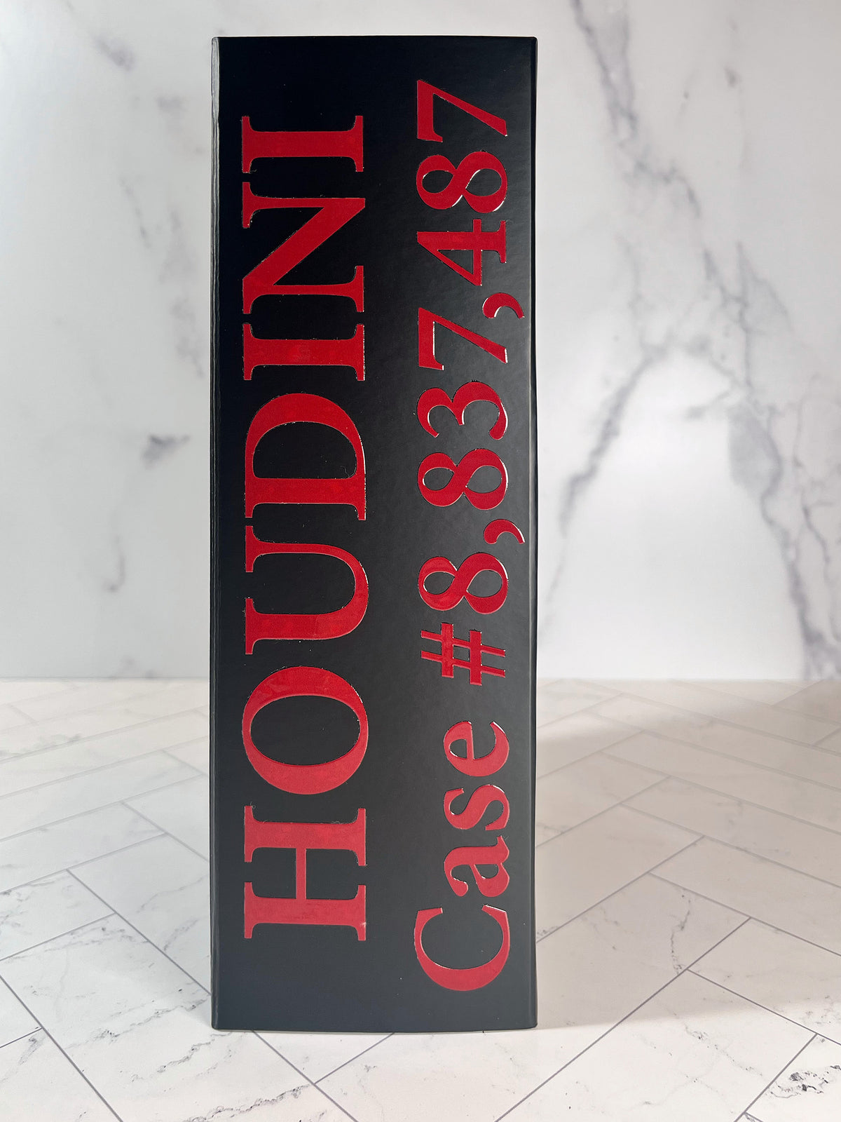 Black box with bold red text reading “The Murder Box Edition” on a tiled surface with a marble-patterned background.