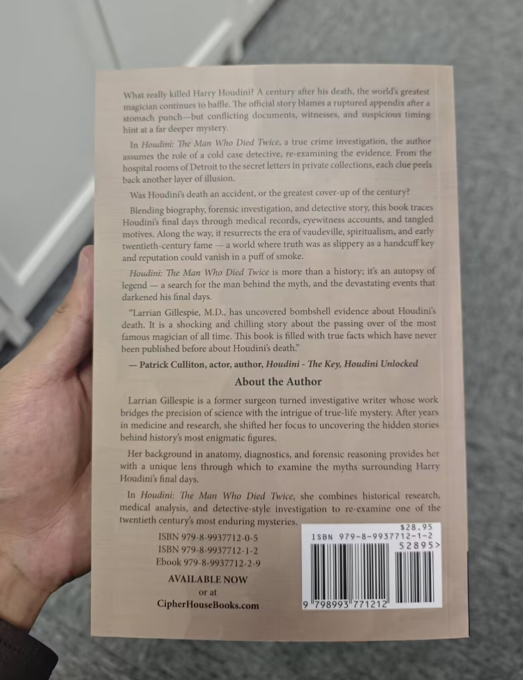 A person holds the Trade Paperback Edition of "Houdini: The Man Who Died Twice," displaying its beige back cover with summaries, reviews, and a barcode—ideal for true crime enthusiasts curious about Houdini's death.