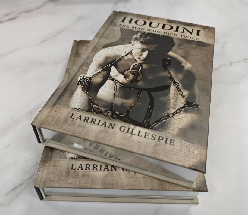 Two Collectors Edition Hardback Shrink Wrapped copies of "Houdini: The Man Who Died Twice" by Larrian Gillespie are stacked on marble, featuring a cover image of Houdini in chains—perfect for true crime and magic history fans.